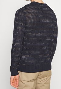 Pull marinière affichant un design en tricot texturé avec des accents dorés et argentés subtils, des poignets côtelés et un col rond.