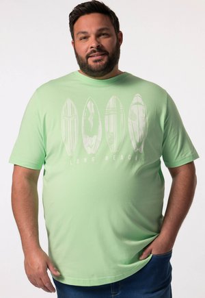 Camiseta de algodón verde claro con un gráfico de tablas de surf y el texto "LONG BEACH". Manga corta y un corte relajado con un escote redondeado.