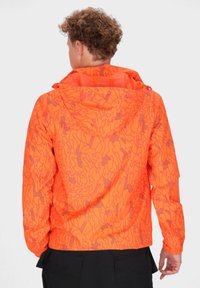 Giacca leggera arancione con un motivo geometrico; presenta un cappuccio, polsini elastici e una silhouette leggermente aderente per il massimo comfort.