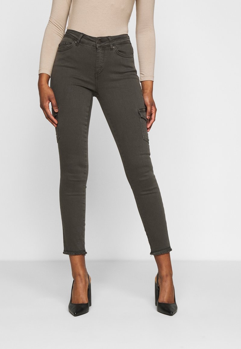 Jean cargo skinny vert olive à taille haute, avec poches avant et ourlets effilochés, confectionné en tissu denim extensible. Associé à des talons noirs.