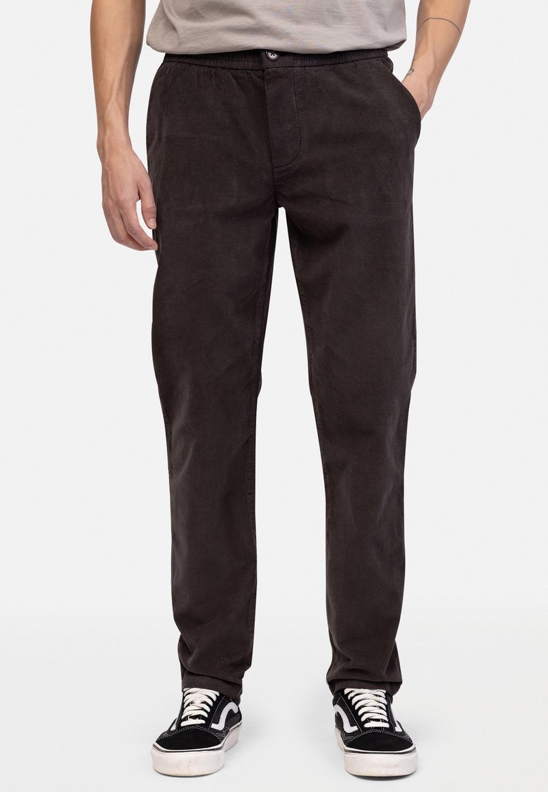 Ciemnobrązowe sztruksowe spodnie z elastycznym pasem, bocznymi kieszeniami i luźnym krojem, zestawione z czarno-białymi tenisówkami.