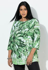 Zielony top w kwiatowy wzór z rękawami do łokcia i szerokim dekoltem. Wykonany z lekkiego materiału o luźnym kroju, zestawiony z czarnymi spodniami.