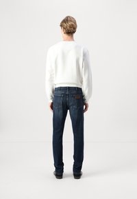 Jeans de mezclilla azul oscuro con un corte recto, que cuentan con dos bolsillos traseros y un parche de cuero marrón. Combinados con un sudadera blanca ajustada.