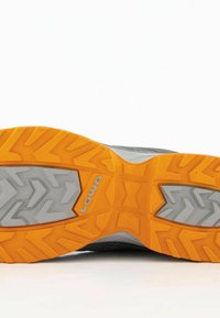 Graue Wanderschuhsohle mit einem strukturierten Muster; verfügt über orangefarbene Gummiakzente und ein hexagonales Profildesign für besseren Halt. Der Markenname "LOWA" ist sichtbar.