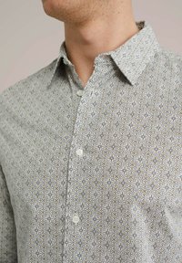 Camisa a cuadros de tela ligera; presenta un patrón de formas geométricas en beige, azul y blanco; con cuello abotonado y botones.