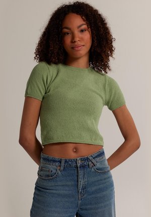 Green knitted crop top with short sleeves, round neckline, and ribbed hem, paired with high-waisted blue denim jeans.