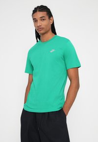 Πράσινη βαμβακερή μπλούζα με κοντά μανίκια, στρογγυλή λαιμόκοψη και μικρό λευκό λογότυπο Nike στην αριστερή πλευρά του στήθους. Λείος υφασμάτινος σχεδιασμός, κανονική εφαρμογή.