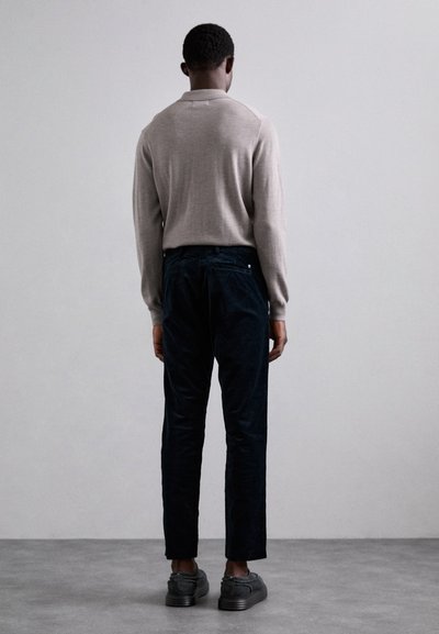 Beige knit pullover with a classic collar, paired with navy corduroy pants featuring a back pocket and black sneakers.