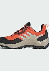 Trail running sko med en svart, orange och grå syntetisk ovandel, med en strukturerad sula och reflekterande silverdetaljer.