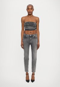 Hallitatud hall ilma õlgeteta top "Moschino Jeans" tekstiga, kombineeritud istuvate hallide teksadega. Mudel kannab musti terava nina kaabu. Puhtas taust.