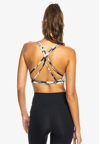 Sostén deportivo con un patrón floral azul, que cuenta con un diseño de espalda con tiras y una tela suave. Combinado con leggings negros de cintura alta.