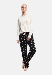 Hvid langærmet top med bjørn grafik; sorte pyjamasbukser med beige bjørn print. Løs pasform, blødt stof, elastisk talje.