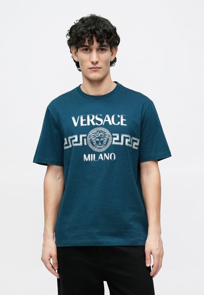 Tirkīza kokvilnas T-krekls ar uzrakstu "VERSACE MILANO" un Medūzas emblēmu ar grieķu atslēgas rakstu kontrastējošā krāsā. Īsās piedurknes.