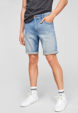 Pantalones cortos de mezclilla azul claro con dobladillos enrollados, diseño de cinco bolsillos y cierre de botón. Combinados con zapatillas altas blancas y calcetines a rayas.