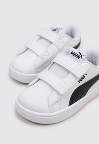 Sneakers in pelle bianca con accenti neri, dotati di due fasce in Velcro, punta rotonda e interno imbottito per il comfort. Logo PUMA visibile.