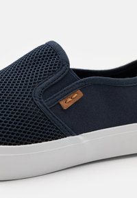 Námořnické slip-on boty s vrchním dílem z prodyšné síťoviny, pevnými textilními akcenty, bílou gumovou podrážkou a hnědým koženým logem na boku.