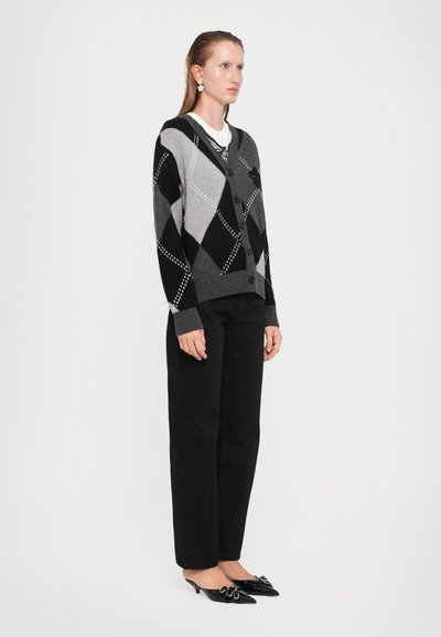 Svart og grå argyle strikket cardigan med knappeåpning, båret over en hvit skjorte; kombinert med svarte straight-leg bukser og svarte mules.