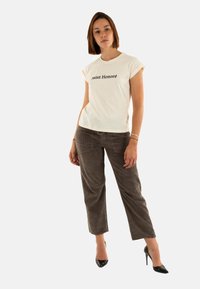 T-shirt bianco a maniche corte con testo "Saint Honoré" in nero, abbinato a pantaloni in velluto a coste marrone scuro e tacchi alti neri.