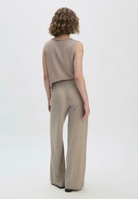 Beiger, ärmelloser, kurzes Oberteil mit Rundhalsausschnitt; kombiniert mit fließenden, weiten Hosen aus einem ähnlichen Stoff und in derselben Farbe, glatte Textur.