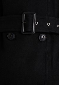 Zwarte wollen jas met een brede riem met een rechthoekige gesp, twee ronde knopen en metalen accenten voor het afsluiten. Zachte textuur en gestructureerd ontwerp.