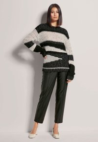 Gestreifter Pullover in Schwarz-Weiß mit lockerer Passform, gestrickter Textur und langen Ärmeln; kombiniert mit schwarzen tapered Hose aus Kunstleder und cremefarbenen High Heels.