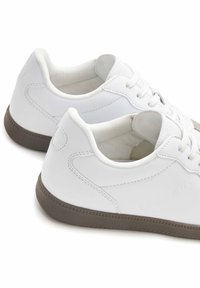 Weiße Leder-Sneaker mit niedrigem Schnitt, runder Zehenpartie, flachen Schnürsenkeln und einer braunen Gummisohle mit strukturierten Details.