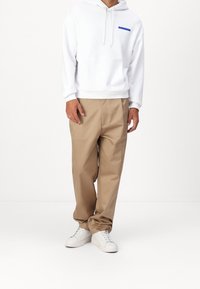Sudadera blanca con capucha y logo azul, combinada con pantalones beige y zapatillas blancas. Todas las prendas presentan un diseño sencillo y casual.