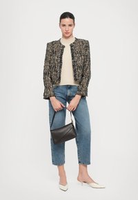 Textuur gemêleerd jasje met franjes, beige trui, lichtblauwe high-waisted jeans en een zwarte driehoekige handtas. Witte puntige hoge hakken.