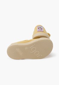 Geel schoeisel met een gestructureerde rubberen zool, voorzien van een speelse aap patch met het label "Made in Spain." Schoon, minimalistisch ontwerp.