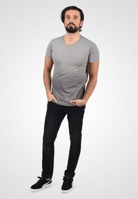 Grå t-skjorte med kort erme og tett passform, kombinert med svarte jeans og svarte sneakers. Antrekket har et uformelt og stilrent utseende.