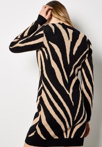 Strickkleid mit einem schwarz-beigen Zebra-Streifenmuster, langen Ärmeln, rundem Ausschnitt und gerippten Bündchen. Strukturierter Stoff.