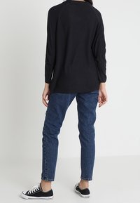 Schwarz langärmliges Oberteil mit lockerer Passform, strukturiertem Stoff und Raglanärmeln, kombiniert mit blauen Jeans in mittlerer Waschung mit engerem Schnitt und schwarzen Sneakers.