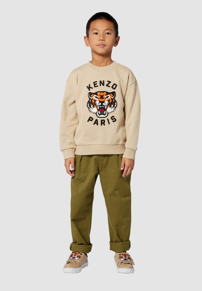 Felpa beige con grafica di tigre nera e arancione e testo "KENZO PARIS". Pantaloni verde oliva e scarpe beige con design di tigre.