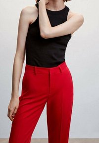 Débardeur noir à côtes associé à un pantalon tailleur rouge. Le pantalon présente une texture lisse et un design à jambes droites avec des poches avant.