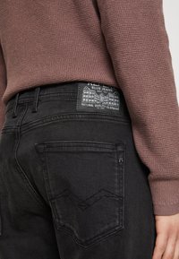 Jeans in denim nero con una vita testurizzata, dotati di una patch con il marchio e due tasche posteriori con un motivo di cucitura a zigzag.