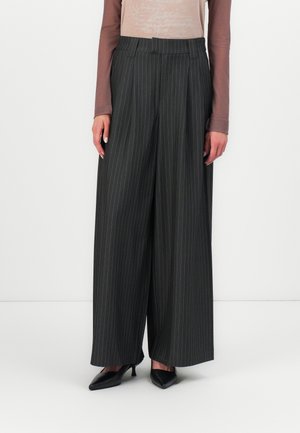 Pantalons à jambes larges en gris foncé avec des rayures blanches. Présentent une taille haute, des plis et un tissu lisse, complétés par des escarpins noirs pointus.