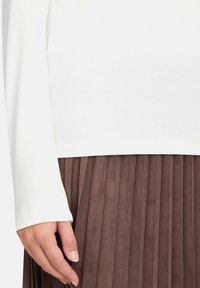 Długi rękaw biały top zestawiony z plisowaną brązową spódnicą. Top ma prosty design, natomiast spódnica charakteryzuje się miękką, teksturowaną powierzchnią.