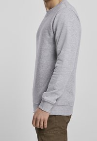 Sudadera gris hecha de un tejido suave y texturizado. Presenta un cuello redondo, mangas largas y puños y dobladillo acanalados. Diseño simple y casual.