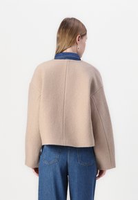Bežna skrajšana pulover s soft tkanino z oversized rokavi in zaobljenim ovratnikom, položen preko kavbojskega srajca. Jeans so modri z zadnjimi žepe.