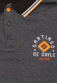 Grijze polo met zwarte kraag en oranje gestreepte accenten. Beschikt over een geborduurd ontwerp met de tekst "Santiago de Chile" in wit en oranje.