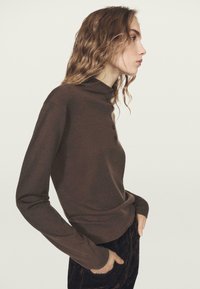 Maglia marrone a maniche lunghe con collo alto e davanti con bottoni, realizzata in un tessuto liscio ed elastico. Silhouette aderente e design minimalista.