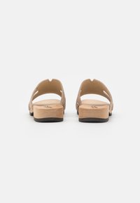 Tan suède sandalen met een open achterkant, met een houten zool en een zwarte rubberen onderkant. Uitsparingen aan de zijkanten zorgen voor meer ventilatie.