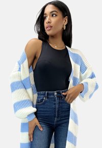 Gestreifter Strickcardigan in weichen Blautönen und Weiß, kombiniert mit einem schwarzen Bodysuit und hoch geschnittenen dunklen Jeans.