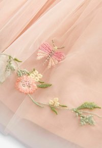 Un tissu en tulle rose présente des broderies détaillées avec des motifs de papillons et de fleurs dans des teintes pastel de rose, jaune et vert.
