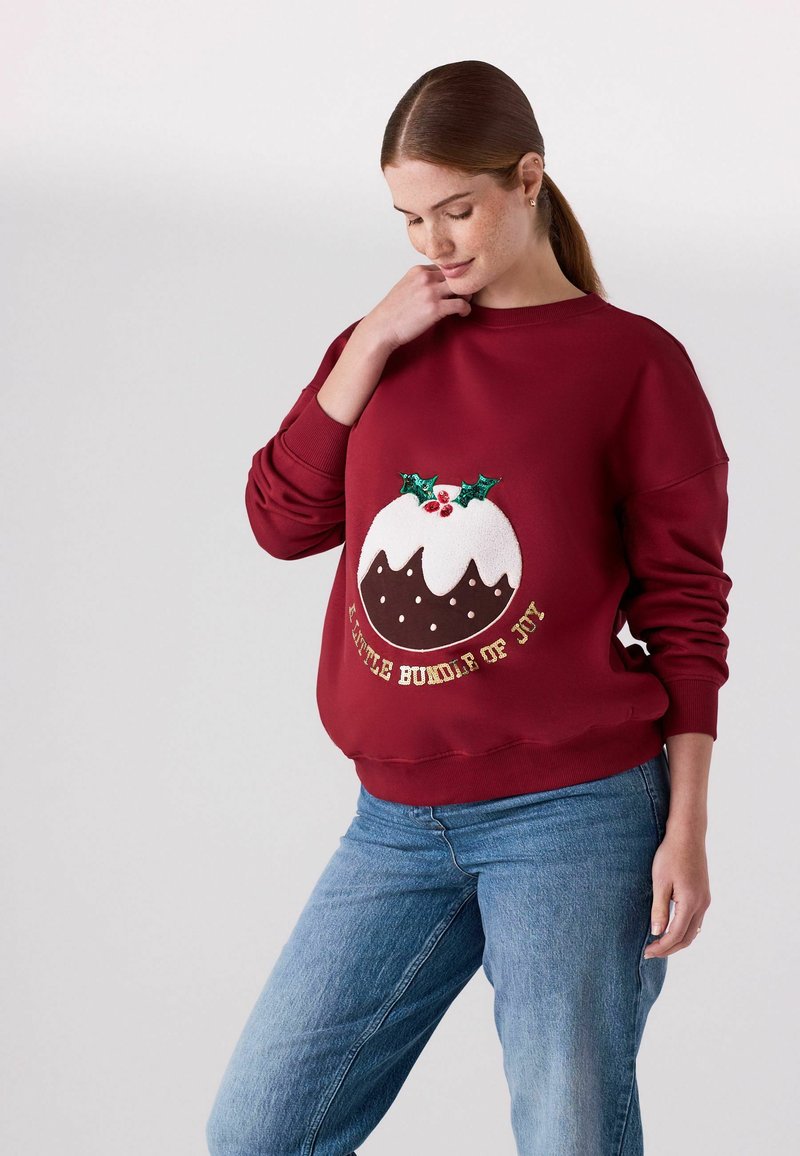 Bordeaux sweatshirt met een geborduurd ontwerp van een kerstpudding met hulst en bessen, en tekst die zegt "Een Klein Bundeltje van Vreugde."