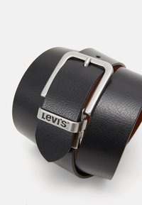 Zwarte leren riem met een zilveren metalen gesp met het Levi's-logo, met een gestructureerd oppervlak en gelaagd ontwerp.