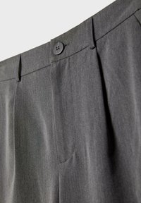 Pantalon de costume gris foncé avec une taille boutonnée et des passants de ceinture, montrant la texture du tissu et les plis devant.