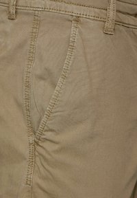 Beige bomullsbyxor med en slät textur, med sydda sömmar och midjeband. Inkluderar en framficka med synlig rynkning.