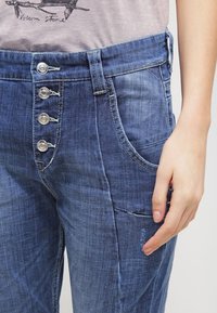 Niebieskie dżinsowe spodnie z wysokim stanem, pięcioma guzikami, bocznymi kieszeniami i lekko postarzonym wyglądem.