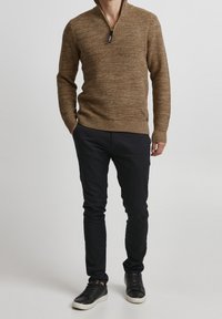 Pull tricoté marron avec un col zippé, assorti à un pantalon noir slim et des baskets noires. Tissu texturé avec des poignets et un ourlet côtelés.